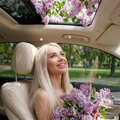 Женщина с букетом сирени в люксовом автомобиле с панорамной крышей
