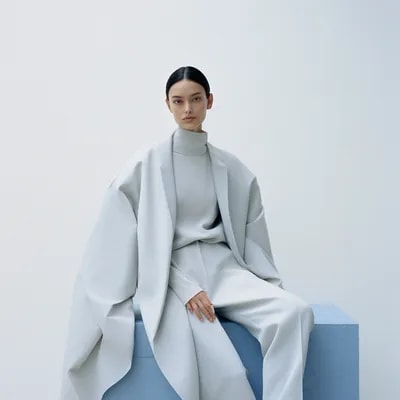 a woman sitting on top of a white cube, official j...