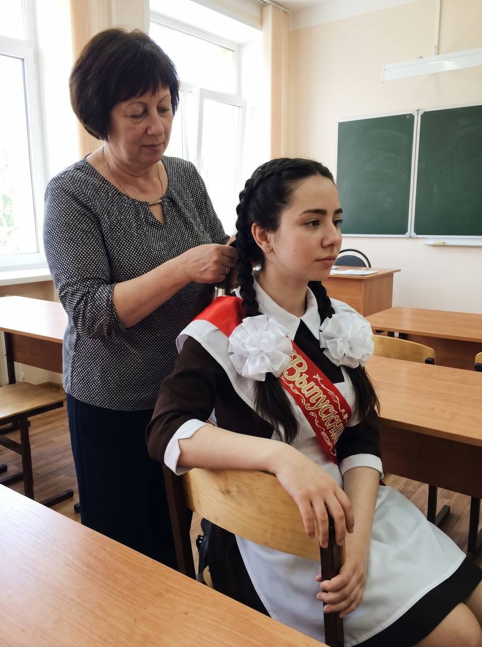 Мама заплетает косы дочери перед выпускным